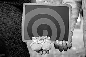 Couple holding writing slate and in hand along with little baby shoes,