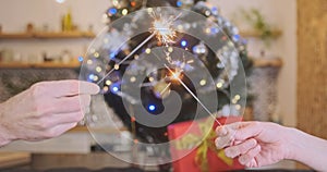 Couple holds burning sparklers in their hands and rejoices in Christmas, waving the lights. Decorated Christmas tree