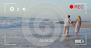 Couple holds hands on beach, viewed on a camera in 4k record mode.