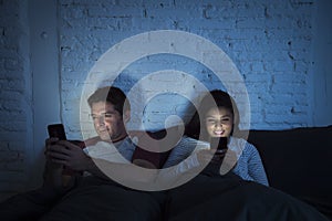 Couple at home in bed late at night using mobile phone in relationship communication problem