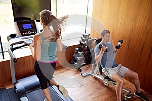 Couple In Home Gym Exercising With Weights And Using Running Machine photo