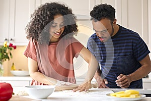 Couple At Home With Man With Down Syndrome And Woman Rolling Dough For Pizza In Kitchen Together