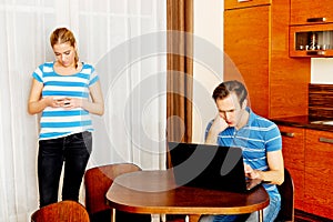 Couple at home, man working on laptop woman using mobilephone