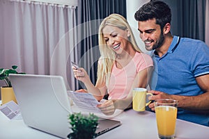 Couple at home paying bills with laptop and credit card