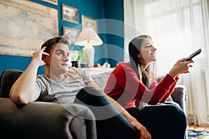 Couple at home watching TV.Remote control fight won by girlfriend.Boyfriend bored by TV program.Watching her favorite show/film.