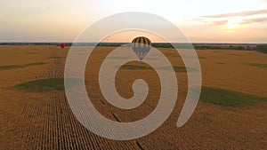 Couple of hot air balloons floating over fields against glowing sky at dusk