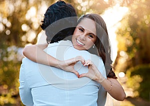 Couple, hug and heart hand gesture in nature for happy, romance and anniversary in garden. Woman, man and love shape in