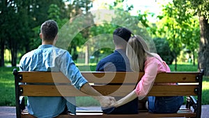 Couple hugging on bench, woman secretly holding hand of other man, betrayal