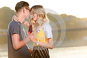 couple hugging and drinking beverage with two plastic straws from one bottle on river beach