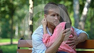 Couple hugging at park, boyfriend texting message another girl, betrayal