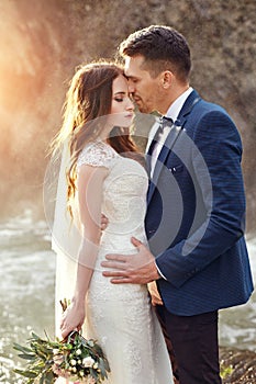 Couple hugging at sunset, lovers couple kissing in sunset. Wedding ceremony outdoors. Beautiful bride and groom with bouquet of f