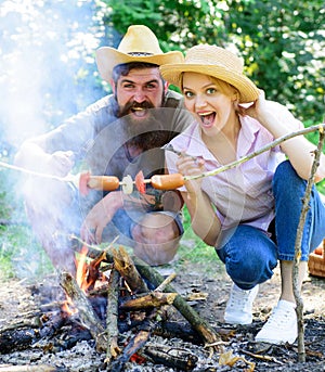 Couple hungry tourists roasting sausages on sticks nature background. Couple in love camping forest roasting sausage at