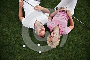 A couple, husband and wife lie on the golf course and relax after the game