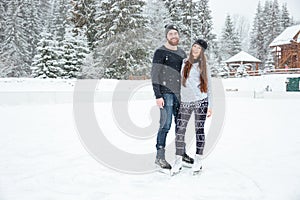 Couple in ice skates hugging and looking at camera outdoors