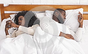 Couple ignoring each other after argue, using smartphones in bed
