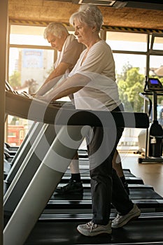 Couple on jogging machine. Senior couple workout in the g