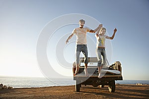 Couple Jumping From Back Of Van Parked By Ocean