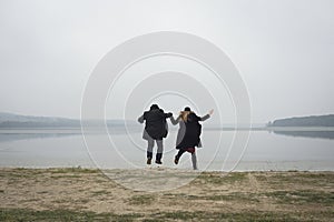 Couple jumping while holding hands on a lake shore