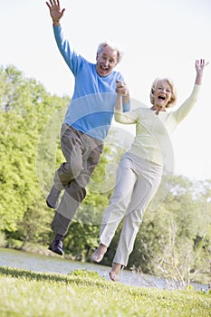 Couple jumping outdoors at park by lake smiling