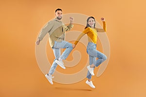 couple jumping shaking their clenched fists in celebration, orange background