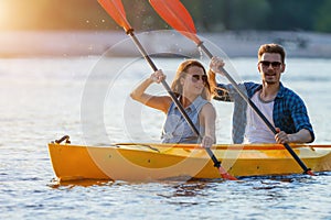 Couple kayaking on river with sunset on background