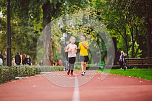 Couple of kids boy and girl doing cardio workout, jogging in park on jogging track red. Cute twins runing together. Run children,