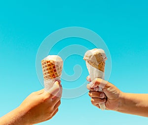 Couple kids hands holding ice cream cones against blue sky background in summer vacation. Summer food, summertime joy