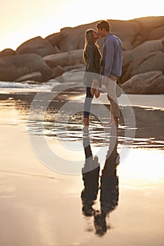 Couple, kiss and love at sunset by water, ocean wave and peace for romance in relationship. People, affection and