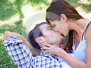 Couple, kiss and picnic on grass for love, bonding and connection on holiday in park outdoors. Relax, man and woman with