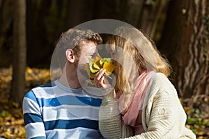 Couple kissing in autumn park hiding behind leaves