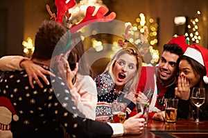 Couple Kissing In Bar As Friends Enjoy Christmas Drinks