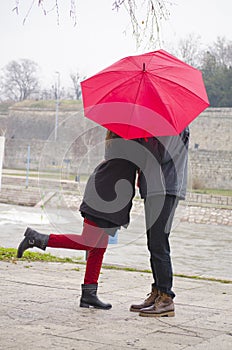 Couple kissing behind a red umbrela