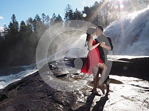 Couple kissing and dancing in a park with a waterfall on the background under the sunlight