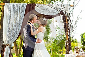 Couple kissing under decorative wedding arch