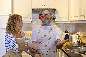 Couple in the kitchen have funny leisure time activity together playing with food during lunch preparation. Happy man and woman