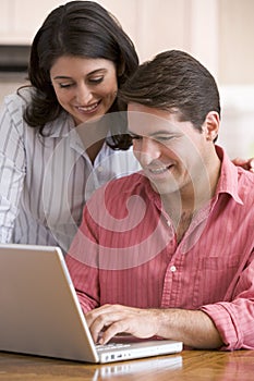 Couple in kitchen with paperwork using laptop