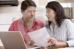 Couple in kitchen with paperwork using laptop