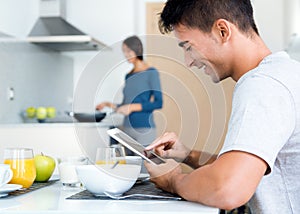 Couple in the kitchen preparing breakfast and browsing internet