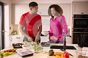 Couple In Kitchen Wearing Fitness Clothing Making Batch Of Healthy Meals For Freezer In Advance