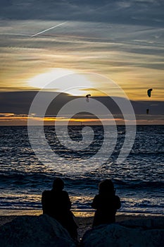 Couple and kitesurfers by the sea at sunset