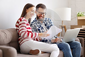 couple with laptop and papers sitting on sofa in room with packed boxes and discussing insurance contract after relocation into ne