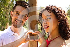 couple of latin lovers leaning on a wooden poster forming a heart with their hands. The man is camouflaging the woman to make her