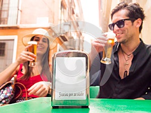 couple laughing drinking beer behind napkin ring that says thank you for your visit in Spanish