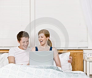 Couple laughing and using laptop in bed