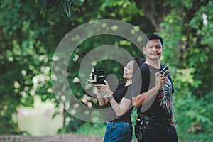 A couple is learning to take pictures with boyfriend teaching his girlfriend about photography in the forest or park