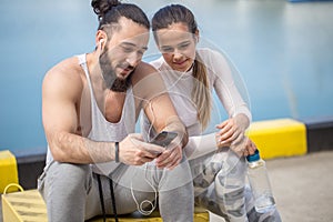 Couple listening to music together using one earphones sitting on pier