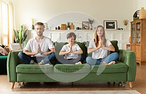 Couple and little son sitting on sofa in lotus position with closed eyes