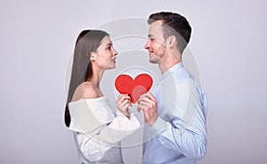 The couple look at each other and hold a red paper heart