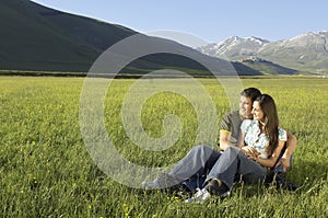 Couple Looking Away While Sitting On Grassy Field