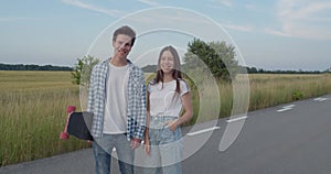 Couple looking at camera, girl poses and talks during a walk with skateboard